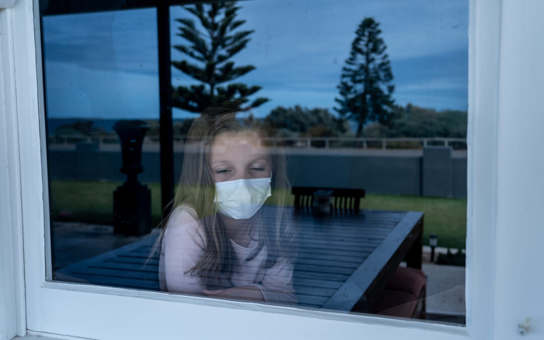 COVID-19 Quarantine. Sad little girl looking through the window feeling lonely during lockdown